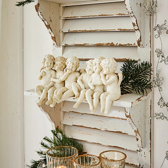 Zes engeltjes op een wit verweerd houten wandrek, gedecoreerd met kerstgroen.