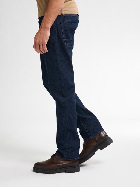Zijaanzicht van een man in een donkerblauwe straight fit jeans met bruine leren schoenen.