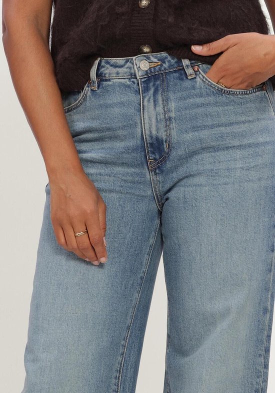 Lichtblauwe wide leg jeans met hoge taille, gedragen door een model met de hand in de zak.