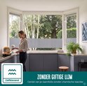 Vrouw kookt in een keuken met grijze kastjes en een erkerraam met horizontale grijze vouwgordijnen. "Zelfklevend".