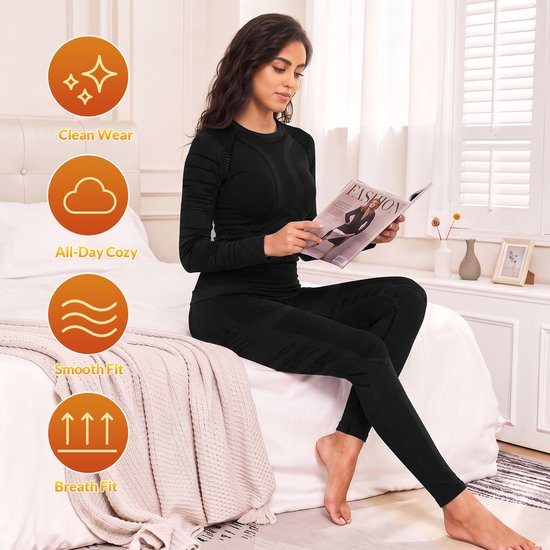 Vrouw op een bed leest een tijdschrift, gekleed in zwarte thermokleding, met iconen voor schone kleding, comfort, soepele pasvorm en ademende pasvorm.