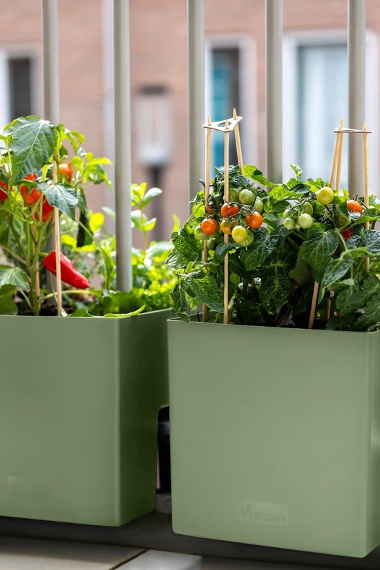 Twee olijfgroene Vercony plantenbakken met paprika- en tomatenplanten tegen een balkonhek.