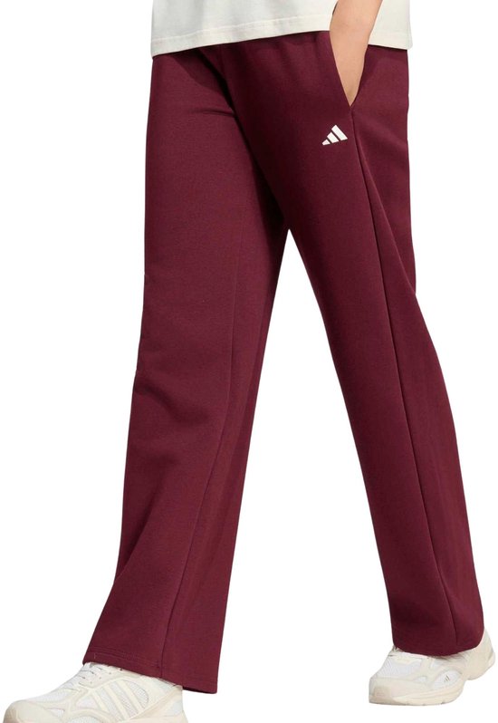 Model draagt een wijde bordeauxrode sportbroek met wit adidas logo op het been.