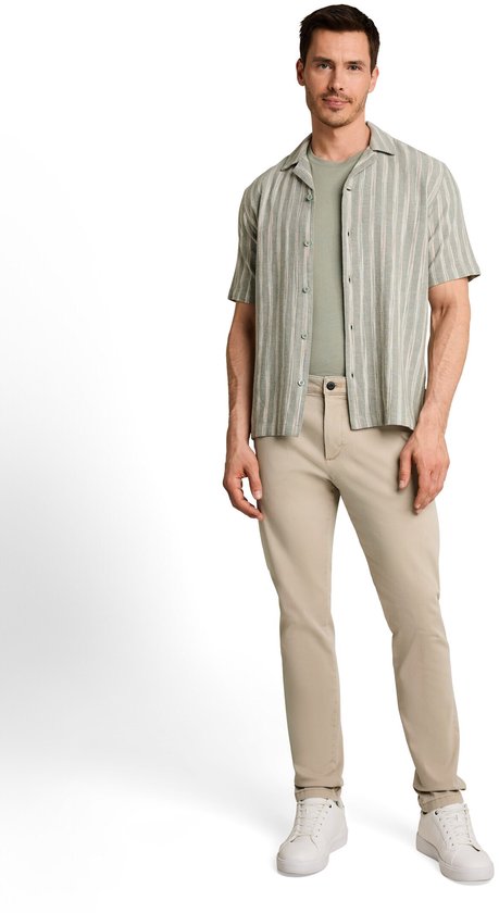 Man in beige chino broek, lichtgroene T-shirt en gestreepte korte mouwen blouse.