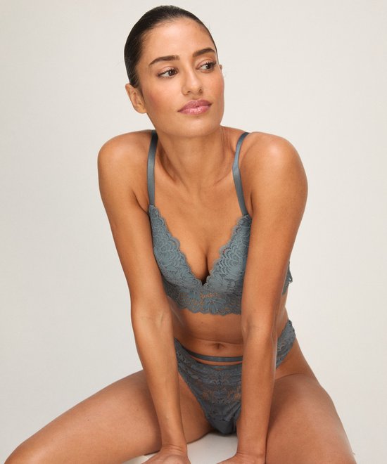 Model draagt een blauwe kanten bralette en bijpassende string met bandjes.