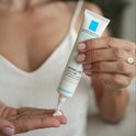 Une femme presse une petite quantité de crème hors du tube La Roche-Posay Effaclar Duo+M dans sa main.