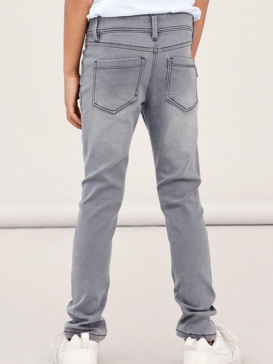 Achterkant van een grijze, aansluitende jeans met opgestikte achterzakken en zwarte stiksels.