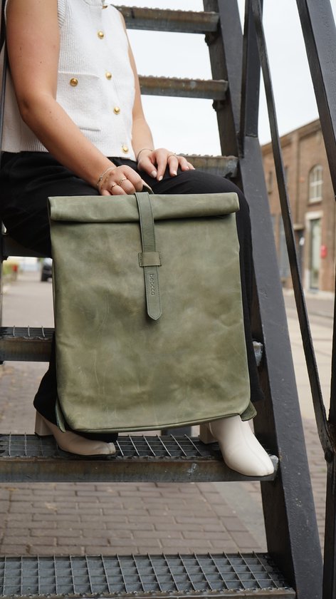 Vrouw met groene leren rol-top rugzak, zittend op een metalen trap.