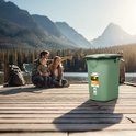 Groene campingtoilet emmer met deksel, op een houten pier bij een meer met familie op de achtergrond.