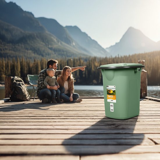 Groene campingtoilet emmer met deksel, op een houten pier bij een meer met familie op de achtergrond.