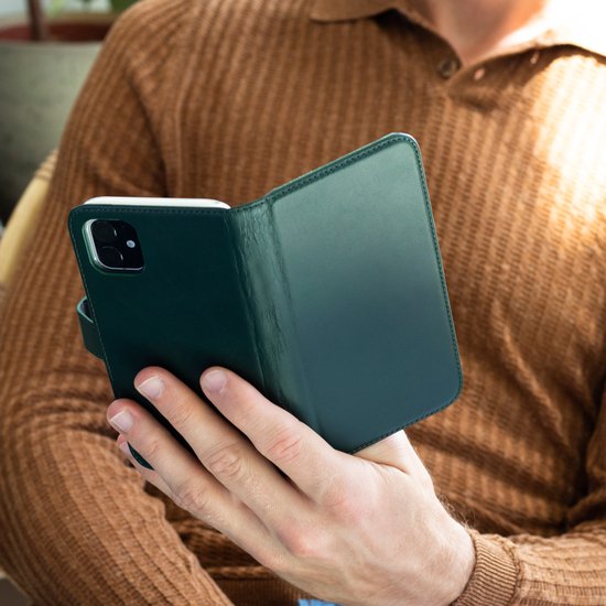 Hand van man met bruine trui die groene Selencia bookcase opent voor telefoon.