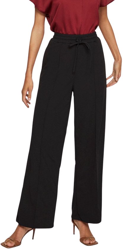 Een vrouw draagt een wijde zwarte broek met hoge taille en koord.