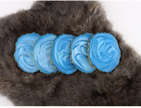 Cinq sous-verres bleus en epoxy avec bordures dorées, posés sur une fourrure grise.