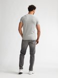 Man met krullend haar, achterkant van een effen lichtgrijs T-shirt met ronde hals en grijze jeans.