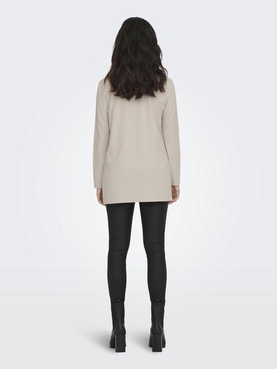 Vrouw van achteren gezien, met lange donkere haren, staand in een lange, beige blazer en zwarte broek.