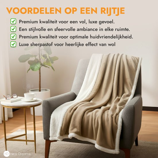 Een taupe plaid met witte sherpa voering, gedrapeerd over een grijze fauteuil. Een bijzettafel met een bril en kopje staan naast de stoel.