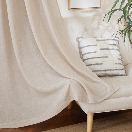 Lichtbeige linnen gordijn voor een fauteuil met decoratieve kussens en een plant.