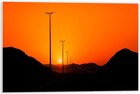 WallClassics - PVC Schuimplaat- Zonsondergang over Weg met Lantaarnpalen tussen Bergen - 60x40 cm Foto op PVC Schuimplaat