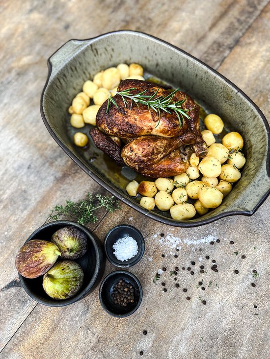 Gegrilde kip met aardappelen, vijgen en kruiden in een groene ovenschaal.