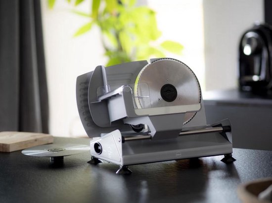 Zilverkleurige vleessnijmachine op een zwarte tafel met gedimd achtergrondlicht.
