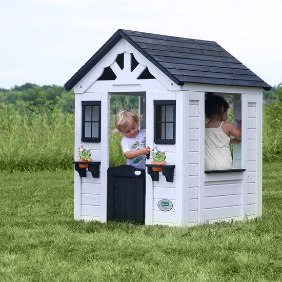 Wit houten speelhuis met zwart dak in de tuin. Twee kinderen spelen erin.