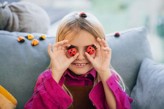 Une fille tenant deux coccinelles rouges devant ses yeux, avec plus de coccinelles en arrière-plan.