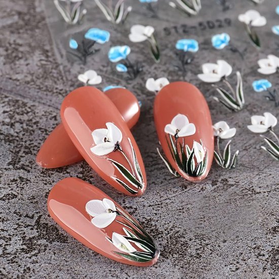 Koraalkleurige nepnagels met witte bloemen en groene bladeren, met transparante nagelstickers op de achtergrond.