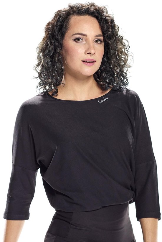 Close-up van een vrouw met krullend donker haar, draagt een zwarte top met ronde hals en 3/4-mouwen. Tekst 'Winshape' op de linkerborst.