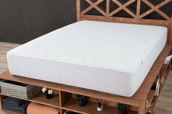 Een witte matrasbeschermer met rondom elastiek, passend op een matras op een bed met houten hoofdeinde.