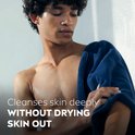Man met donker haar, met een donkerblauwe handdoek om zijn schouders. Tekst: 'Cleanses skin deeply WITHOUT DRYING SKIN OUT'.