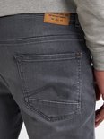 Achterkant van grijze jeans met merklabel 'Crafting Quality Garments' en geborduurde stiksels op de zak.