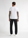 Man met witte t-shirt en zwarte jeans, van achteren gezien.