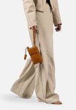 Model met cognac gekleurde telefoonportemonnee met polsbandje, gedragen bij een beige outfit.