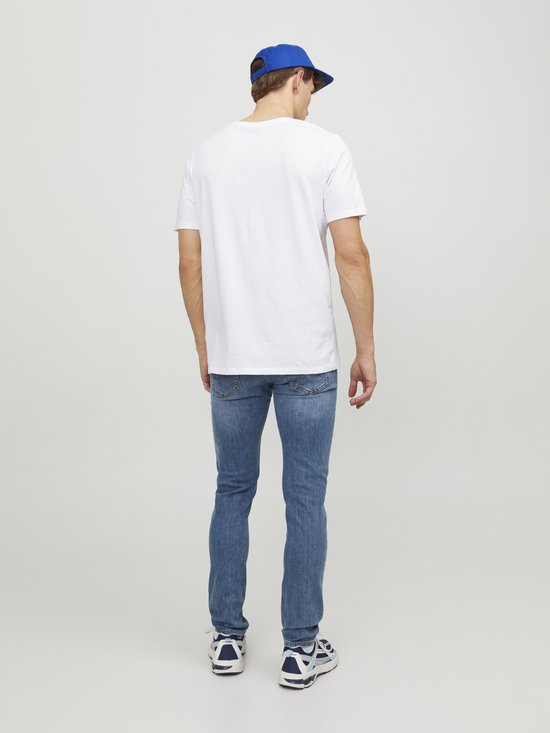 Man in witte t-shirt, blauwe pet en een lichtblauwe skinny jeans.