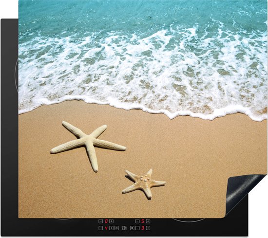 Inductiebeschermer met strand- en zeeafbeelding, zeesterren op zand, branding. Staat op een zwarte inductiekookplaat met rode bedieningsknoppen.