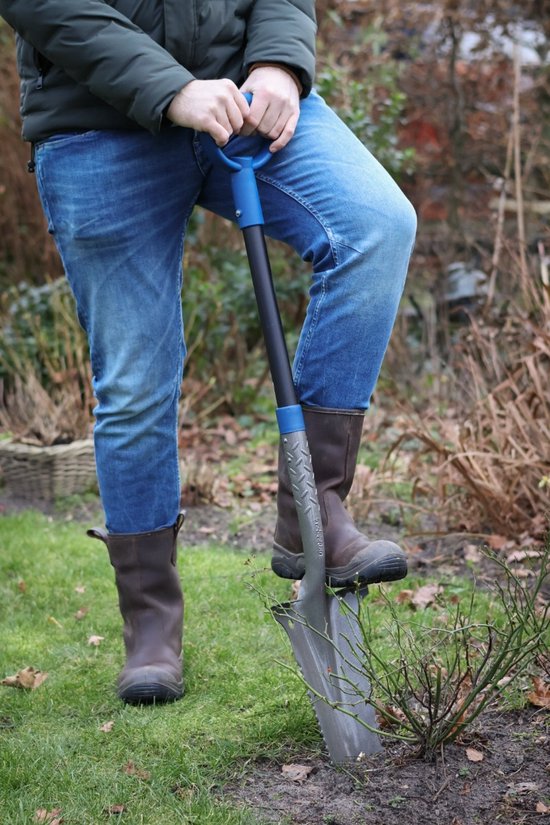 Persoon in spijkerbroek en laarzen gebruikt een schoffel met gekartelde rand in de tuin.