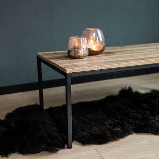 Salontafel met licht houten blad en zwart stalen frame. Twee glazen windlichten met kaarsen erop. Zwart schapenvachtje eronder.