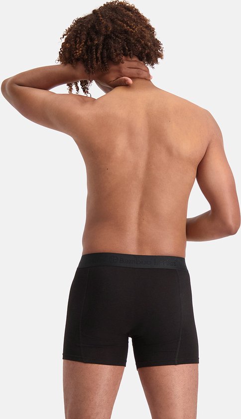 Achterkant van een man met krullend haar die aan zijn nek rust, draagt een zwarte bamboe boxershort.
