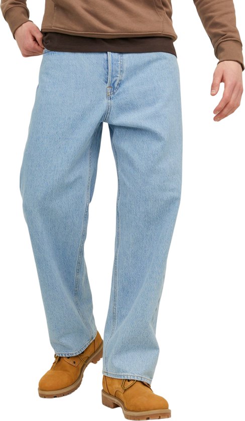 Man in een lichtblauwe loose-fit jeans met bruine laarzen en een bruine hoodie.