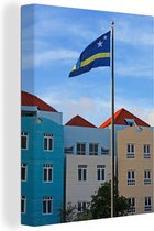 Canvas schilderij 120x160 cm - Wanddecoratie De vlag van Curaçao tussen de gekleurde huizen van Willemstad - Muurdecoratie woonkamer - Slaapkamer decoratie - Kamer accessoires - Schilderijen