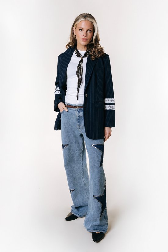 Model draagt een donkerblauwe krijtstreepp blazer, wit T-shirt, jeans met sterren en een sjaal.