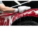 Man wast een rode auto met schuimend autoshampoo.
