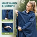 Vrouw met donkerblauwe regenponcho. Details: waterdichte rits en ritszak. Dubbele zijpanelen met drukknopen.