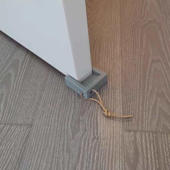 Grijze deurstop met bruin koord, geplaatst onder een deur op een houten vloer.