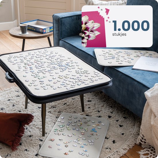 Een woonkamer met een blauwe bank, een tafel met een geopende puzzelmap met 1000 stukjes. Ook losse puzzelstukjes op een mat.