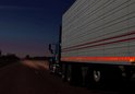 Blauwe vrachtwagen met witte trailer, voorzien van oranje reflecterende contourmarkering op de zijkant.