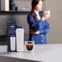 Wit De'Longhi waterfilter met blauwe dop, naast een doos en een espresso kopje.