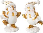 Twee pinguïnornamenten in wit en goud met muts en sjaal op schaatsen, op een witte sneeuwachtige ondergrond.