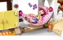 Meisje met roze pet in een LEGO hangmat met roze-witte stippen. Op de achtergrond een raam met muzieknoten.
