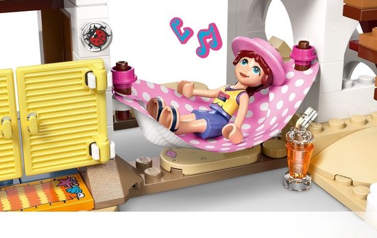 Meisje met roze pet in een LEGO hangmat met roze-witte stippen. Op de achtergrond een raam met muzieknoten.